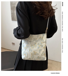 Close-up of white bucket bag featuring blue butterfly embroidery on model's shoulder