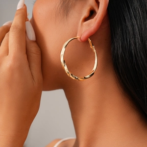 Close-up of model wearing gold twisted hoop earrings with a textured metallic finish