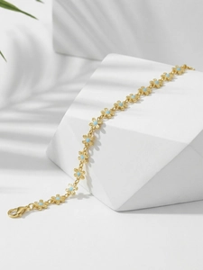 Macro detail of gold flower chain bracelet with light blue floral centers on white stone