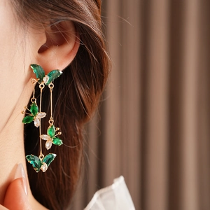 Gros plan de boucles d'oreilles papillon dorées avec strass verts portées par un mannequin