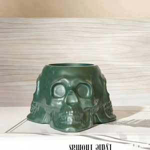 Detailansicht eines glänzend dunkelgrünen Totenkopf-Pflanzgefäßes auf einem Buch