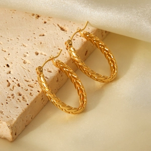 Detailed view of golden twisted C-shaped hoop earrings on elegant silk and stone