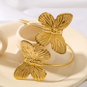 Elegant gold metal double butterfly cuff bracelet on a minimalist ceramic tray