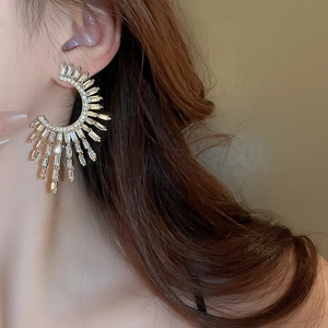 Detailed view of large C-shaped gold earrings with radiating zircon crystals on model