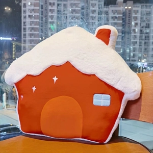 Detailed view of a red house-shaped plush Christmas pillow with white snow-top on a wooden chair