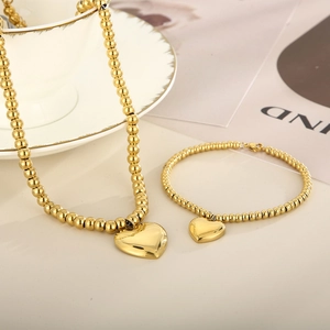 Detailed view of gold beaded necklace and bracelet set with polished heart charms