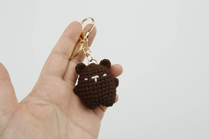 Close-up of a handmade dark brown knitted bear keychain with golden metal ring and chain