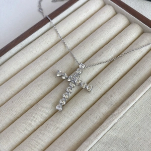 Close-up of a silver cross pendant featuring heart-shaped zircons on a soft velvet box