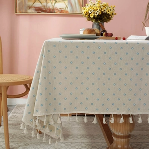 Detailed close-up of beige linen tablecloth with blue floral patterns and tassel edges