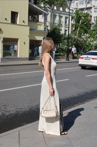 Street style shot of cream long knit dress with beige woven bag and dark pants