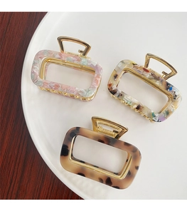Three medium-sized acetate claw clips in floral, colorful, and tortoise patterns on a plate