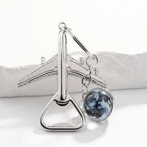 Silver airplane bottle opener keychain with a blue globe pendant on a white stone background