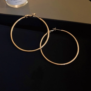 Detailed view of large gold geometric hoop earrings with polished metallic finish on black background