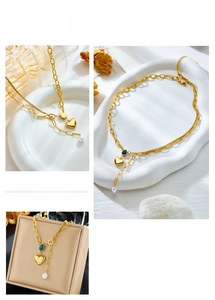 Detail of layered gold heart necklace with blue gemstone and hanging pearl charm