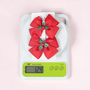 Detail view of 2pcs Christmas red bow hair clips with holly leaf on a digital scale weighing 12.4g