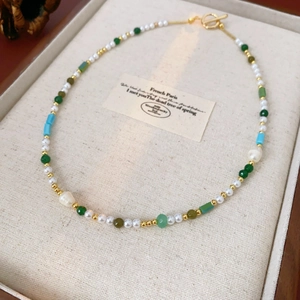 Detailed close-up of pearl necklace with green beads and gold T-bar toggle clasp
