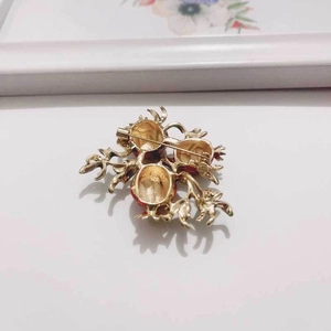 Detailed close-up of a golden pomegranate brooch with vibrant red enamel on a white surface
