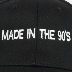 Detailed macro shot of white MADE IN THE 90's embroidery on a black cotton baseball cap