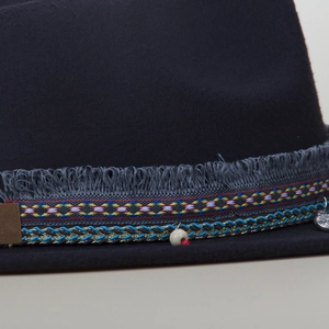 Close-up of ethnic braided band with tassels and metal pendant on wool felt jazz hat