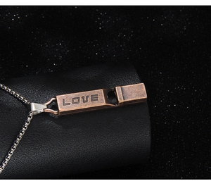 Close-up of vintage bronze whistle necklace with LOVE engraving on black leather stand
