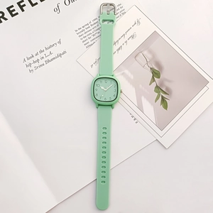 Detail view of light green square watch with white dial on a lifestyle magazine background