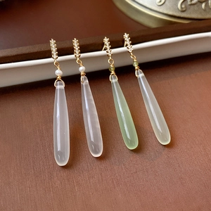 Close-up of teardrop zircon earrings in white and green with gold plating and small pearls