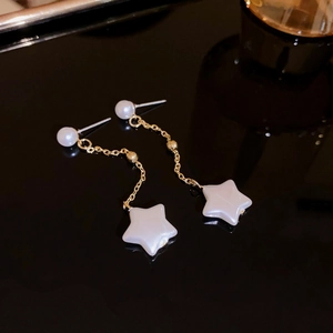 Detailed shot of pearl stud earrings with gold chains and white star pendants on black surface