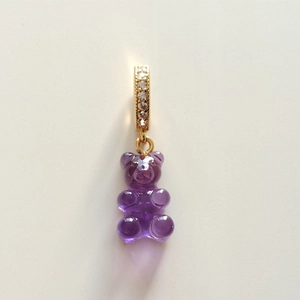 Close-up of purple resin gummy bear pendant with golden diamond-set ring on white background
