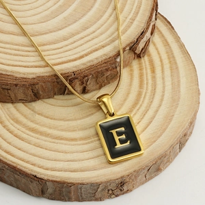 Détail du pendentif lettre E en plaqué or 18k sur une chaîne serpent sur bois