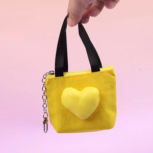 Macro view of yellow canvas heart-shaped mini bag keychain held by hand for scale