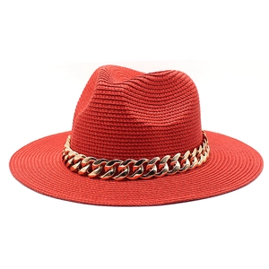 Close-up of red straw fedora hat featuring a chunky gold chain and spiral weave