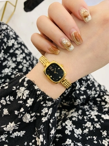 Close-up of elegant gold square watch with black dial and woven metal strap on wrist