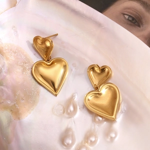 Detailed shot of double heart earrings in 18K gold finish on a pearlescent shell tray