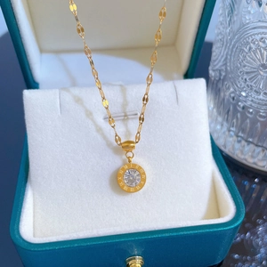 Detailed close-up of golden titanium necklace with roman numeral pendant in teal jewelry box