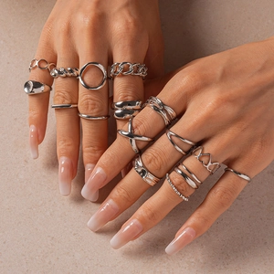 Detailed view of a 16-piece silver alloy geometric ring set on model hands with sand background