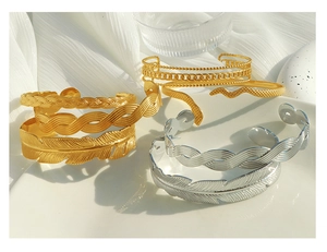 Detailed close-up of 18K gold plated Cuban chain and boho feather textured bracelets