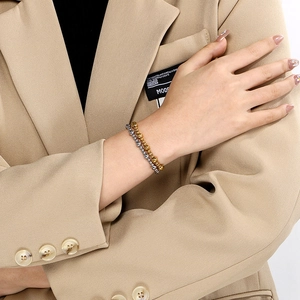 Gros plan de bracelets à billes dorées et argentées portés avec un blazer kaki chic