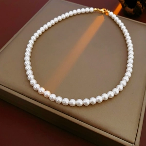 Détail d'un collier de perles blanches rondes avec fermoir doré sur socle beige