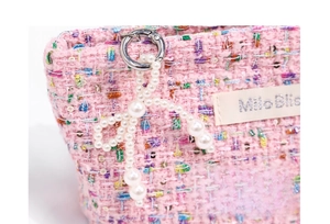 Close-up of pink tweed fabric with a pearl bow charm and Milo Bliss woven brand label