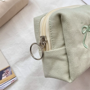 Macro detail of mint green twill makeup bag showing metal ring zipper and bow embroidery