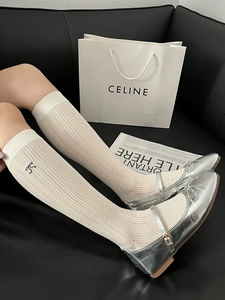 Detail of off-white ribbed knee-high socks featuring small black bow embroidery and silver shoes