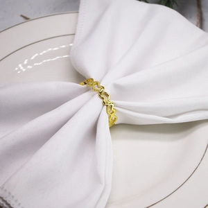 Elegant gold metal heart-shaped napkin ring on white fabric napkin and luxury plate