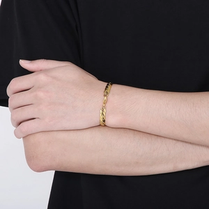 Detail of gold-plated stainless steel Cuban link bracelet on model's wrist with black attire