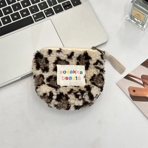 Flat lay of plush leopard print coin purse with zipper and square label on white desk