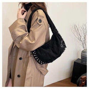 Détail du sac hobo en daim noir avec rivets et patch cœur porté sur un trench-coat
