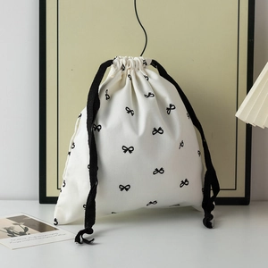 Close-up of white drawstring storage bag with black bow patterns and braided ropes