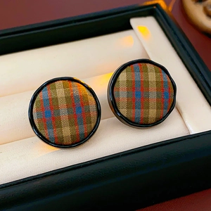 Close-up of circular plaid fabric earrings with classic tartan patterns in a gift box