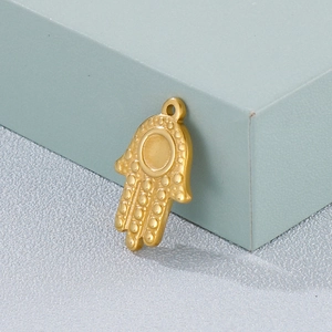 Golden Hamsa hand pendant with textured surface on a minimalist display stand