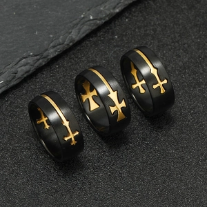 Detail of three black and gold stainless steel cross rings on dark volcanic rock
