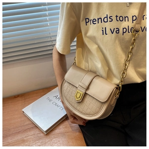 Close-up of beige saddle bag featuring faux crocodile texture and gold shield hardware